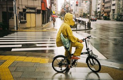 Man in yellow raincoat with bicycle on street during rainy season