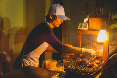 Male chef cooking food on barbecue in illuminated restaurant