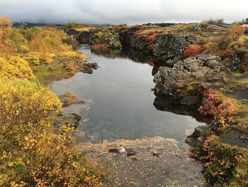 Scenic view of lake by rock formation against cloudy sky at pingvellir national park