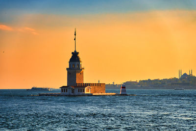 Lighthouse by sea against sky during sunset