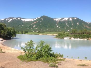 Scenic view of lake by mountain against clear blue sky