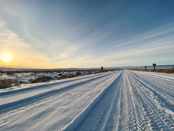 Tire tracks on snow covered field against sky