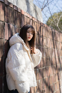 Portrait of young woman standing against wall