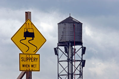 Warning sign and water tower against cloudy sky