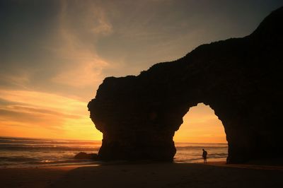 Silhouette rock formation on beach against sky during sunset