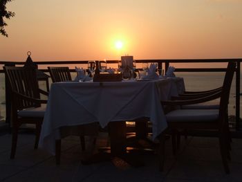 Empty chairs and tables at restaurant against sea during sunset