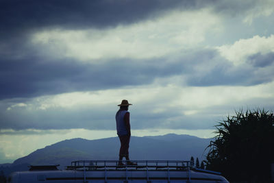 Man standing on built structure against cloudy sky