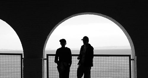 Boys standing at arch window by sea against clear sky