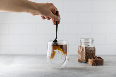 Woman stirs instant coffee in glass mug with boiled water on grey stone table