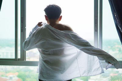 Rear view of man standing by window