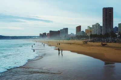 People on beach by sea against sky in city