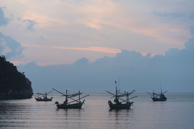 Fishing boats in sea against sky during sunset