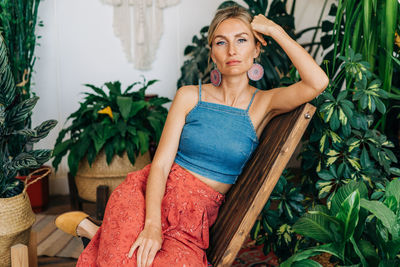 Portrait of a young beautiful woman sitting on a wooden chair in a greenhouse.