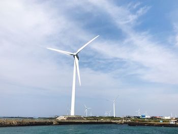 Low angle view of windmills by sea against sky