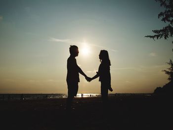 Silhouette couple holding hands while standing against sky during sunset