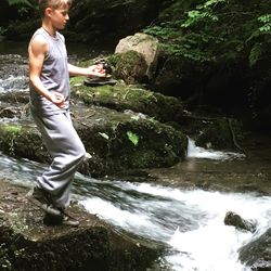 Side view of young man standing by waterfall