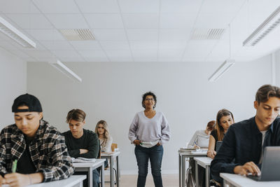 Portrait of female teacher with hands in pockets standing amidst students