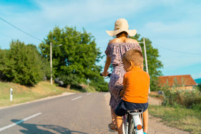 Rear view of mother sitting with son on bicycle