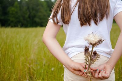 Rear view of woman holding flower while standing on field