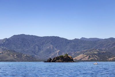 Scenic view of sea and mountains against clear blue sky