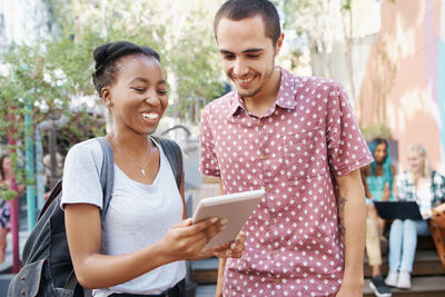 Smiling friends looking at digital tablet in campus