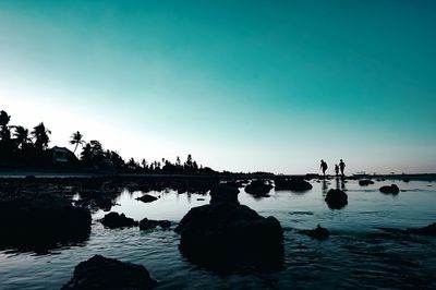 Silhouette rocks in lake against clear sky