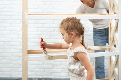 Girl painting wooden structure at home