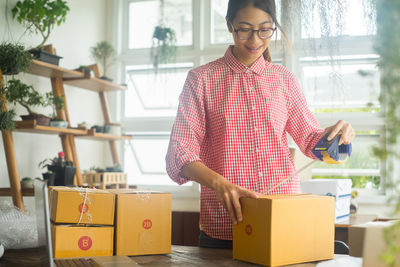 Young woman sticking adhesive tape on cardboard box at home