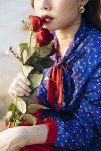 Midsection of woman touching rose to lips