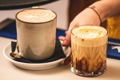 Couple of cappuccino with foam served by the hand of a girl at a bar counter, mug and drinking glass