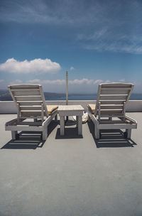 Empty chairs on beach against sky