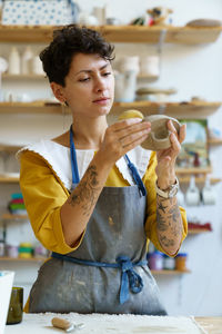 Inspired woman using sponge to absorb water on clay kitchenware, visiting ceramics workshop