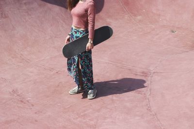 Low section of woman holding skateboard while standing at skateboard park
