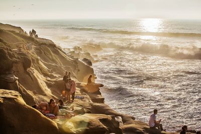 High angle view of people relaxing on rock formations by sea