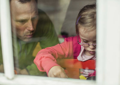View of father and daughter looking down through window