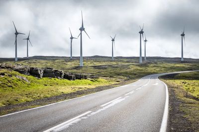 Road by windmills against sky