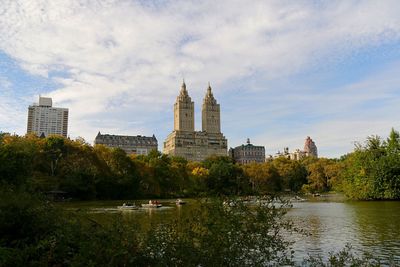 View of buildings by river against cloudy sky