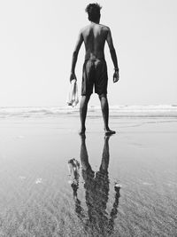 Rear view of shirtless man standing on beach against sky