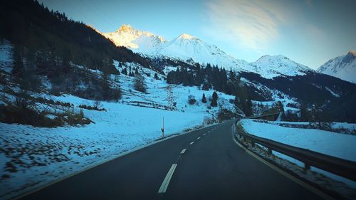 Road by snowcapped mountains against sky during winter