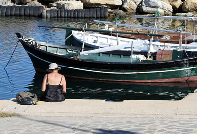 Rear view of woman sitting by boats moored at sea