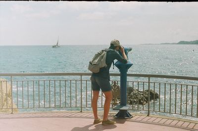 Rear view of man looking through binocular by sea against sky