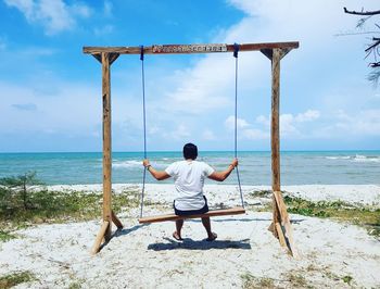Rear view of man on swing at beach