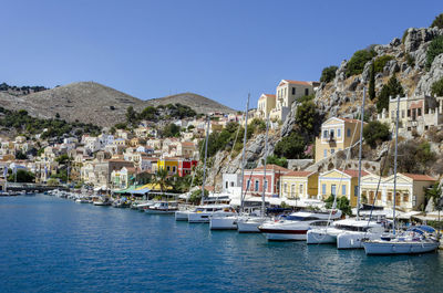 Sailboats moored on river by buildings against clear blue sky