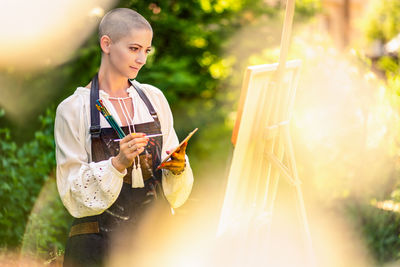 Beautiful woman relaxing while painting an art canvas outdoors in her garden. creativity concept.