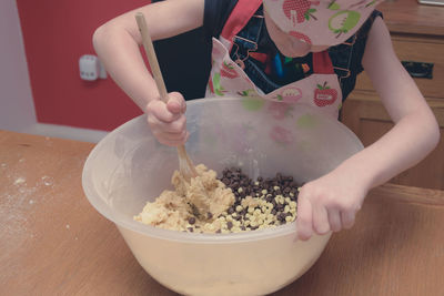 Girl wearing apron mixing flour in container on table at home