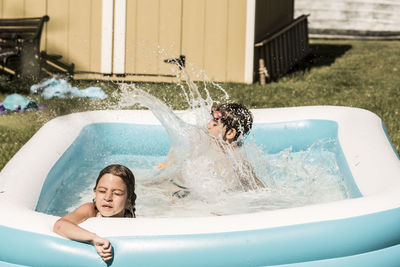 Playful siblings in wading pool at lawn