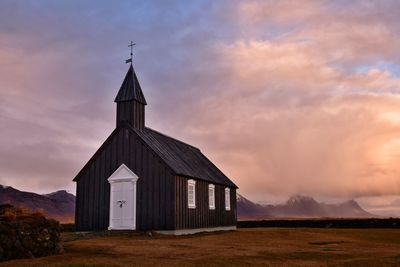 Building on field against sky during sunset