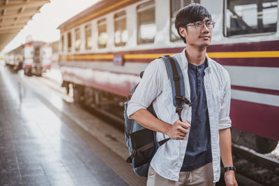 Young man standing by train at railroad station