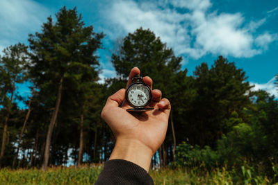 Cropped hand of person holding pocket watch against trees