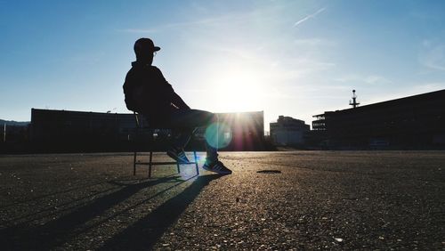 Silhouette man sitting on sidewalk in city against sky